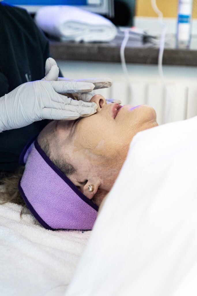 A woman relaxes while receiving a facial treatment with a soothing face mask, likely incorporating LED light therapy for enhanced skin rejuvenation.