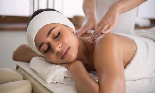 A person lying face down on a massage table with a therapist's hands gently applying pressure to their back.