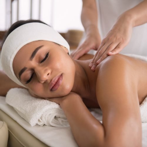 A person lying face down on a massage table with a therapist's hands gently applying pressure to their back.