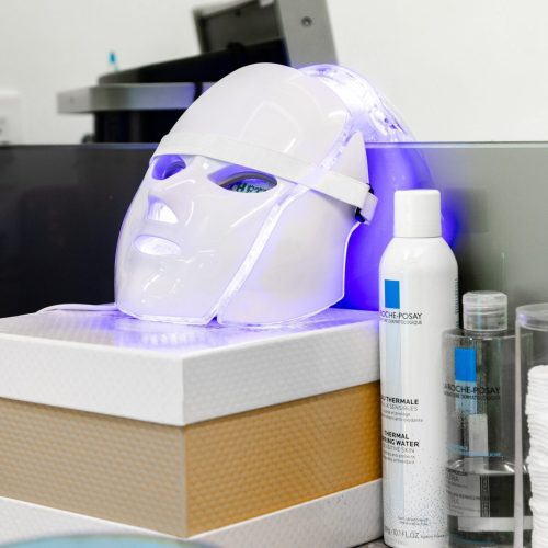 A futuristic LED light therapy mask rests on a counter surrounded by skincare products, promising a revitalizing facial experience.